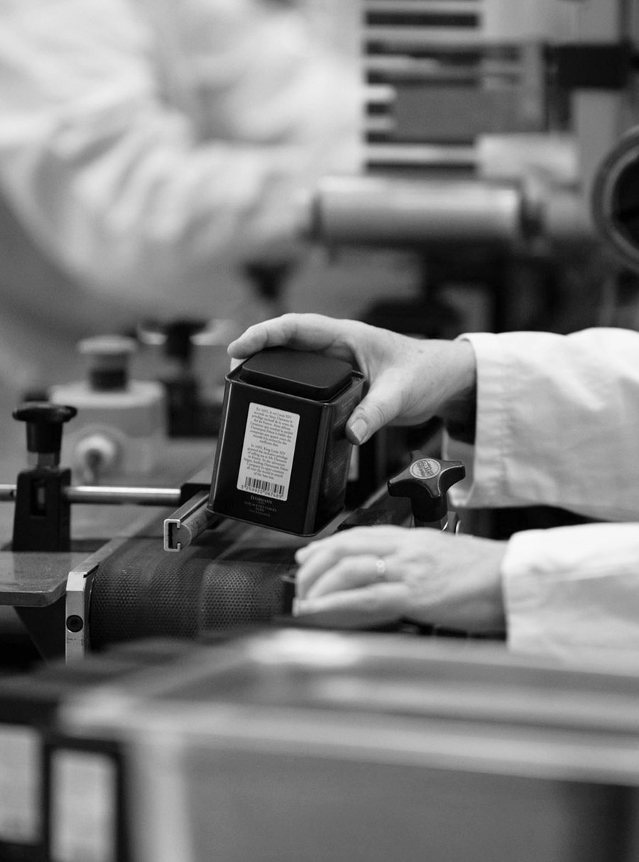 Black-and-white photograph of a worker handling a Dammann Frères tea tin during packaging