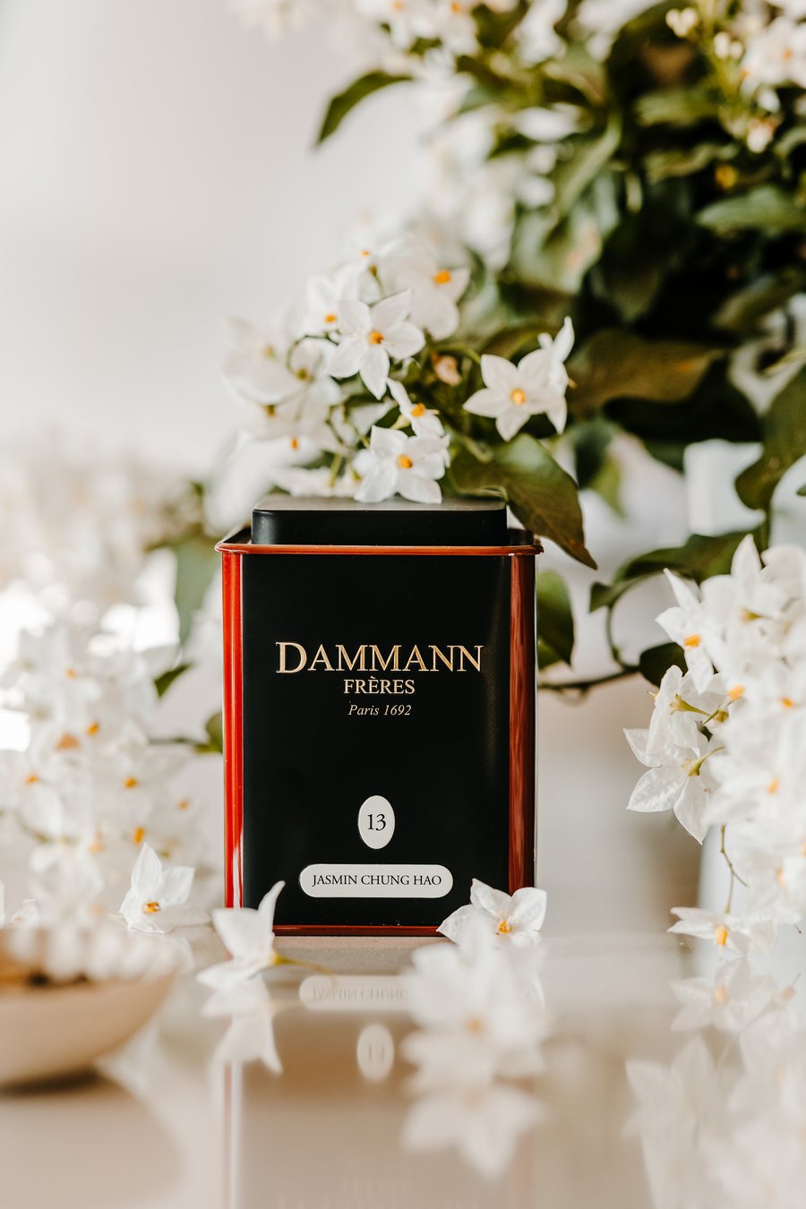 A Dammann Frères Jasmin Chung Hao tea tin surrounded by white jasmine flowers